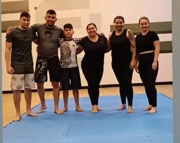 Alunos e alunas de jiu-jitsu reunidos no tatame azul depois do treino